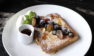 A decadent French Toast with assorted berries, powdered sugar and maple syrup.