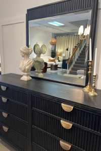 a black dresser/mirror with reeded doors and brass half circle hardware